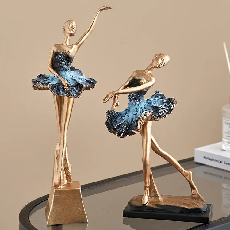 Two blue ballet dancer resin sculptures with gold poses, blue tutus, on black bases