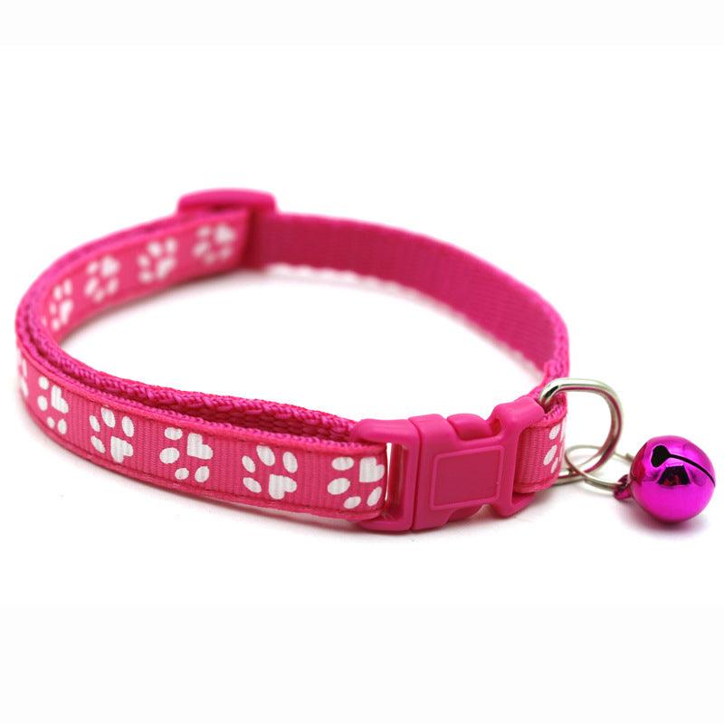 Fuchsia pink pet bell collar with white paw-print pattern, plastic buckle, and bell