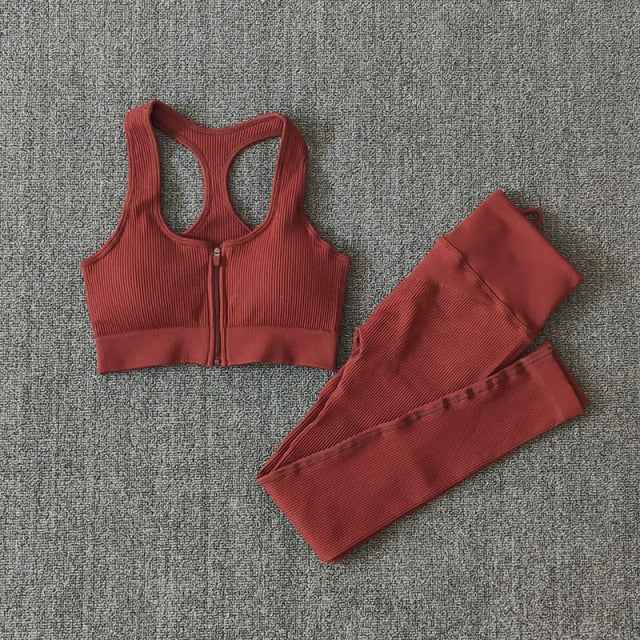 Rust red seamless yoga set with zip-front sports bra and ribbed leggings, flat lay.